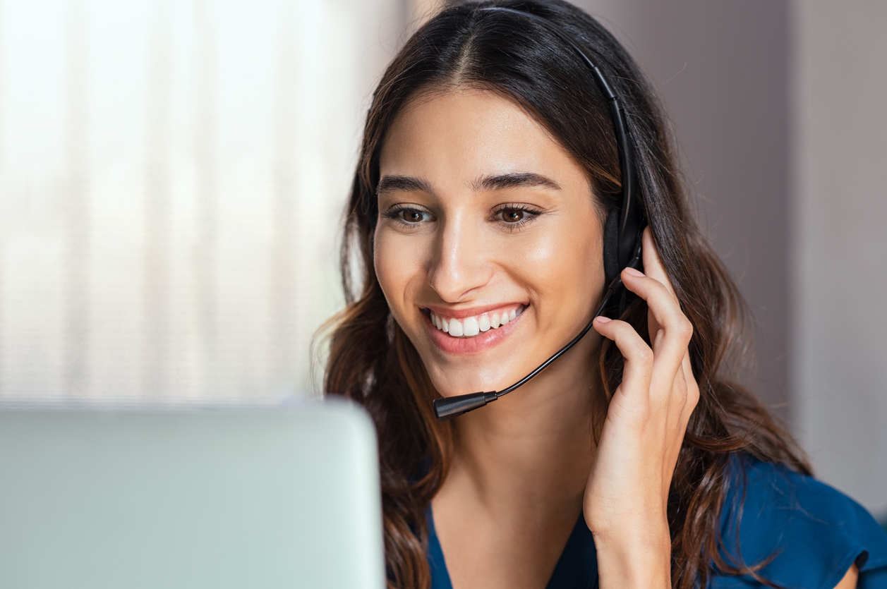 Smiling woman using laptop while talking to customer on phone. Consulting corporate client in conversation with customer using computer on desk. Service desk consultant talking in a call center and working on laptop.