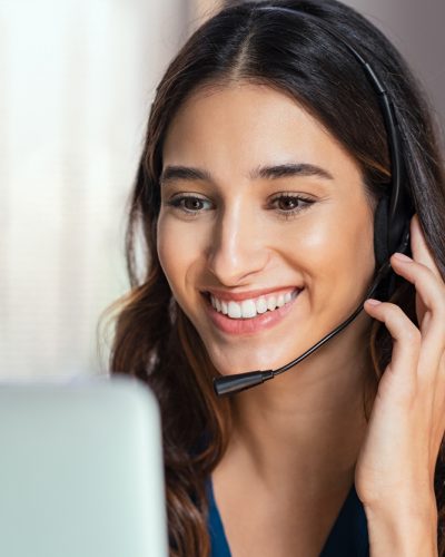 Smiling woman using laptop while talking to customer on phone. Consulting corporate client in conversation with customer using computer on desk. Service desk consultant talking in a call center and working on laptop.