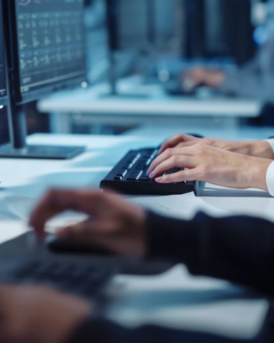 Close Up Hands Shot of a Technical Support Specialist of Software Engineer Working on a Computer in a Dark Monitoring and Control Room. He types on Keyboard and Moves the Mouse.